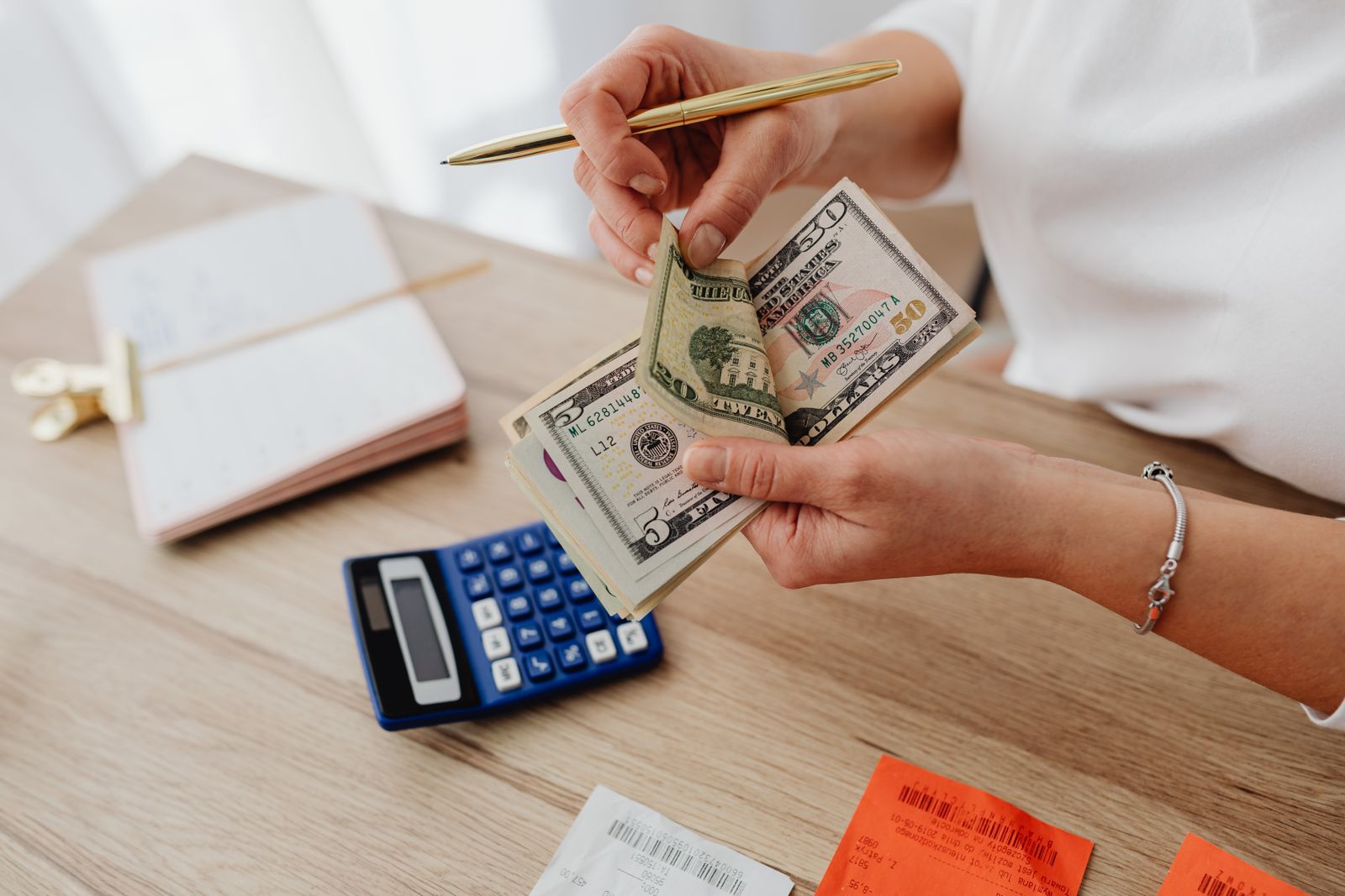 Hands counting US dollar bills beside receipts and a calculator