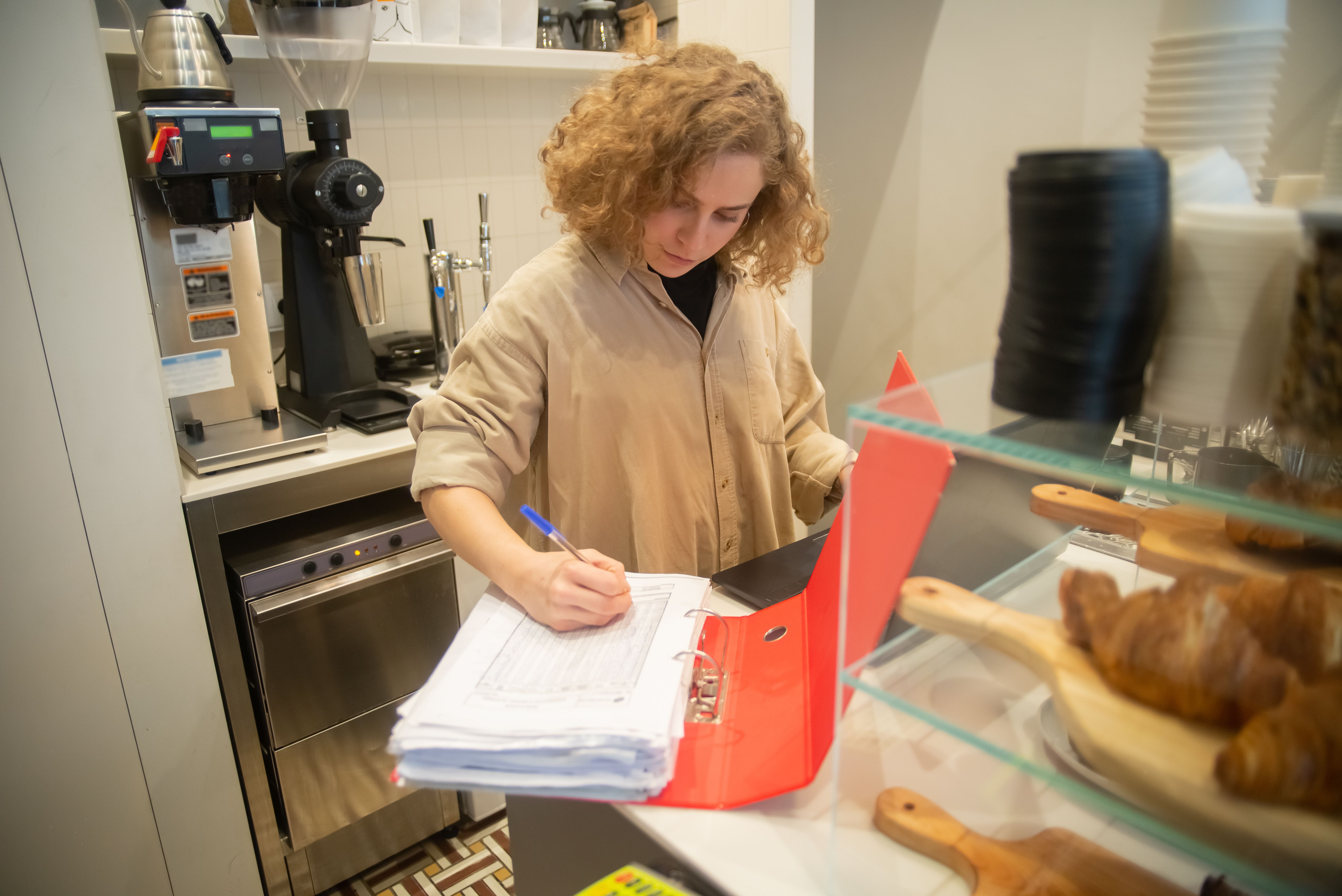 Woman reviewing paperwork in a red binder behind a café counter.