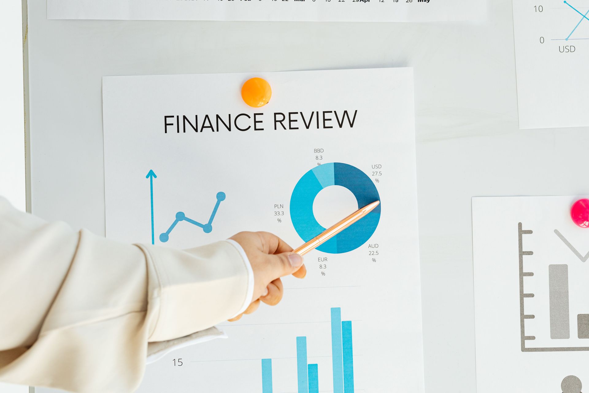 A hand points with a pen to charts on a printed finance review